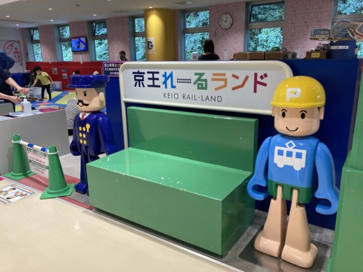 緑色のベンチの両脇にトミカのキャラクターのてっちゃんの人形が立っている