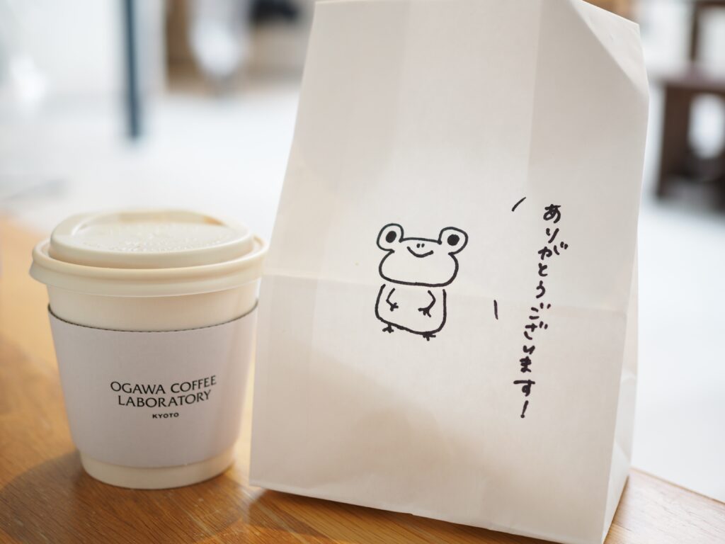 テイクアウト用のコーヒーカップと手書きの絵が描かれた紙袋